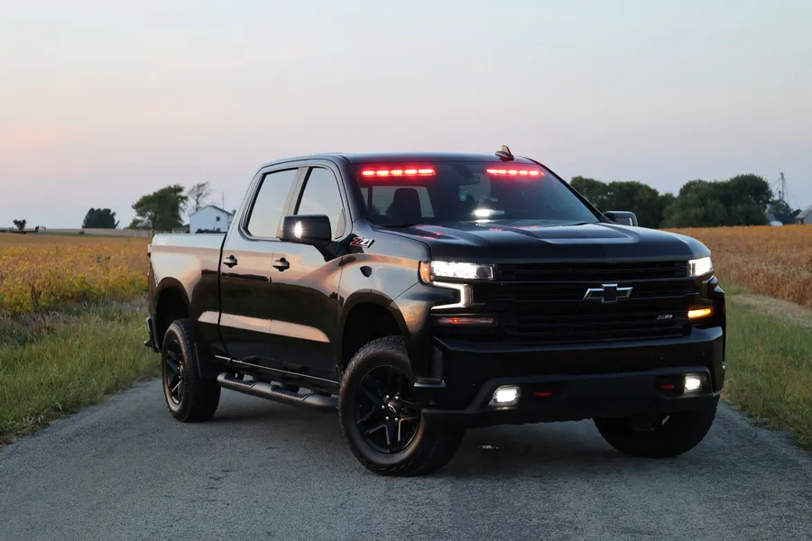 A black pickup used as a brush unit at dusk, fitted with red LED warning lights along the windscreen header and grille.