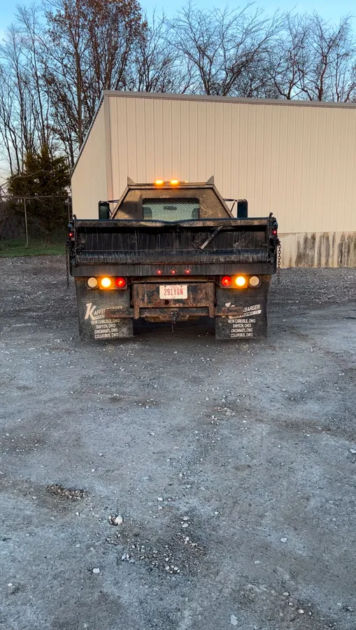 The rear of a dump-bed work truck photographed head-on, with amber warning lights lit along the headache rack at the top of the bed and amber and red lights lit either side of the number plate.