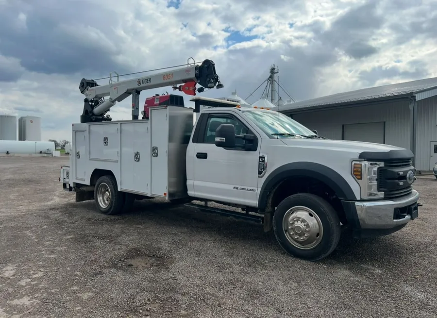 A white service truck fitted with custom toolboxes and a hydraulic-operated air compressor.