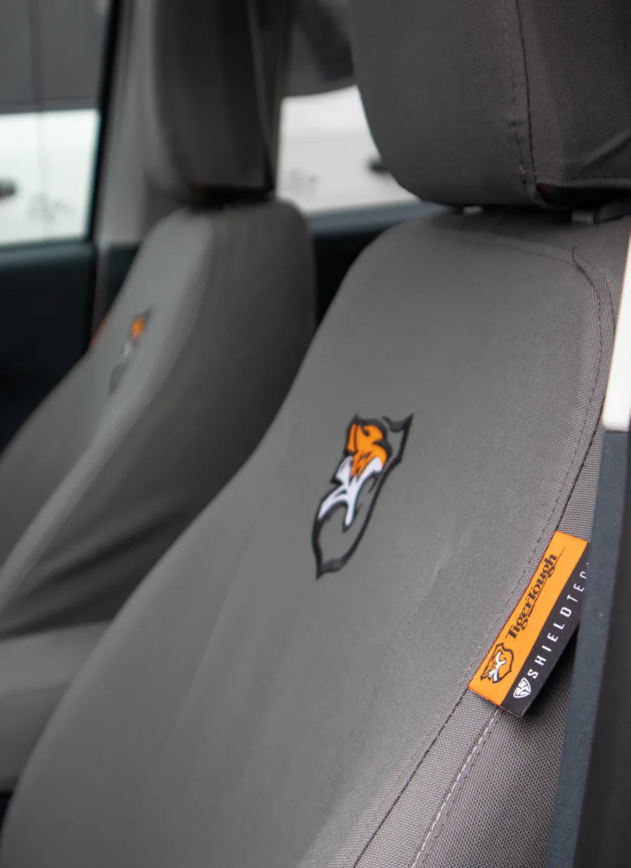 A grey cover on a pickup seat with the TigerTough emblem embroidered on the seat back and an orange TigerTough tag reading ShieldTech at its edge.