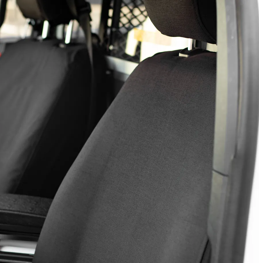 A black Tactical cover on the front seat of a patrol vehicle, the mesh of the prisoner partition visible behind it.