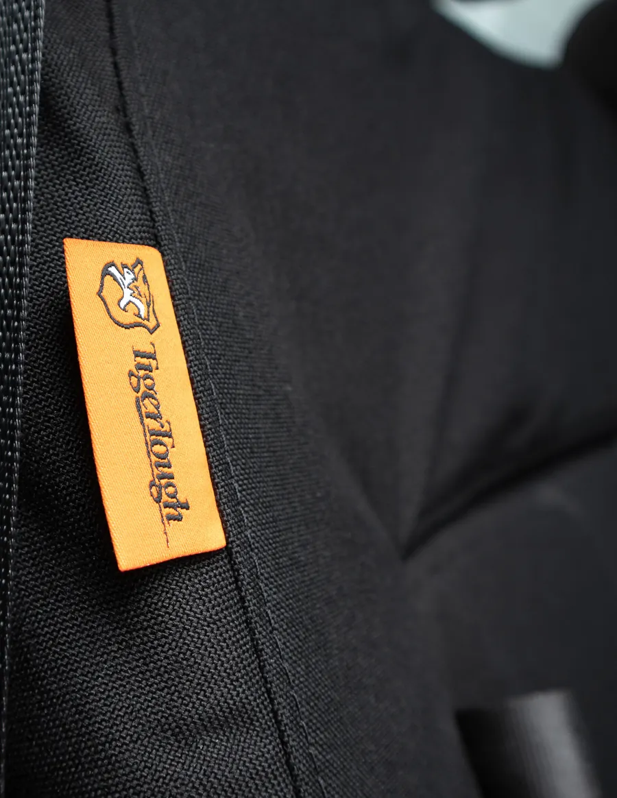 The orange TigerTough tag sewn into the seam of a black cover, the weave of the Cordura visible around it.