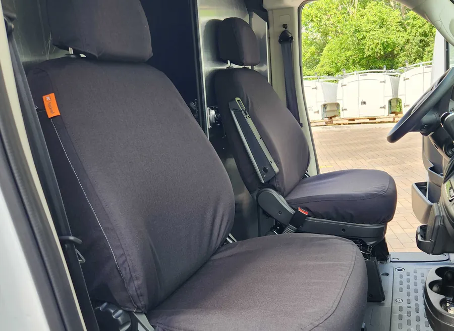Dark TigerTough covers on both front seats of a delivery van, the orange tag on the seat side.